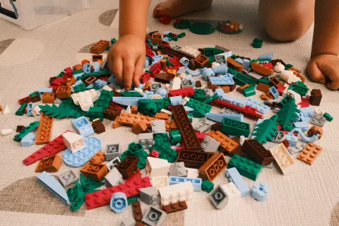 A colour photo of a pile of Lego bricks spread out on the floor. The hands of a young child are visible picking bricks out of the pile.