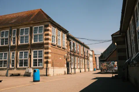 A photo of a school in the midday sun There are no people in the photo. To the right of the photo, a shadow is cast by the building nearest to the photographer.