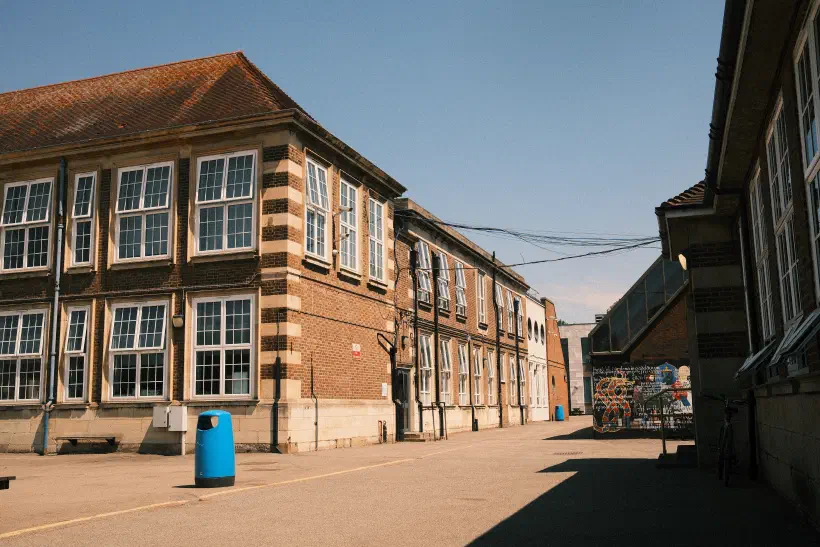 A photo of a school in the midday sun There are no people in the photo. To the right of the photo, a shadow is cast by the building nearest to the photographer.
