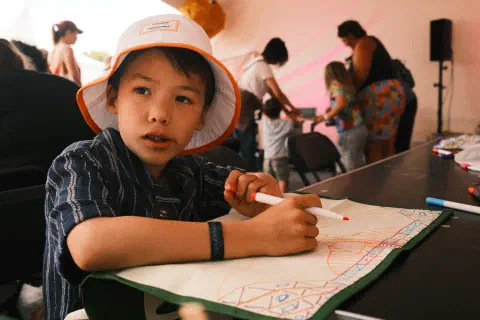 A boy looks off to his right, in his hand a felt tip pen, in front of him an upturned tea-tail on the tea-tail he has been drawing a pattern
