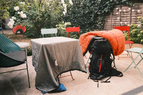 Two sleeping bags put out to air in a garden, they are draped over two square garden tables, in the background overly exposed greenery indicates it's a sunny day